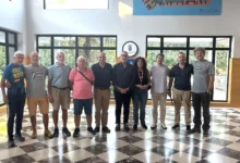 Representantes de las entidades participantes en el II Circuito Local de Carreras Populares de Jerez posan juntos en una sala con grandes ventanales.