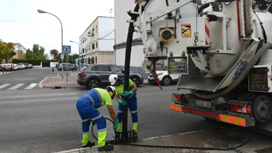 Dos operarios con ropa de trabajo de alta visibilidad limpian un imbornal junto a un camión de saneamiento en una calle de Jerez.