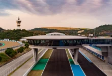 Vista elevada de un edificio acristalado sobre la pista del Circuito de Jerez, con una torre al fondo y zonas de asfalto a ambos lados.