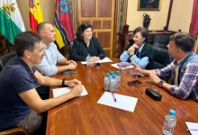 Cinco personas reunidas alrededor de una mesa de madera con documentos, botellas de agua y banderas al fondo.