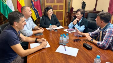Cinco personas reunidas alrededor de una mesa de madera con documentos, botellas de agua y banderas al fondo.