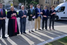 Siete hombres con vestimenta formal, entre ellos uno con indumentaria religiosa negra y fajín fucsia, permanecen de pie al aire libre sosteniendo papeles.