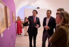 Visitantes observan obras enmarcadas durante la inauguración de la exposición ‘Le Tricorne’ en una sala de paredes blancas y moradas.
