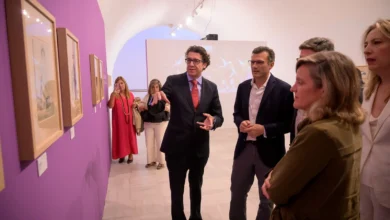 Visitantes observan obras enmarcadas durante la inauguración de la exposición ‘Le Tricorne’ en una sala de paredes blancas y moradas.