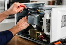 Manos utilizando un destornillador en el interior de un horno microondas abierto, con componentes y cables visibles.