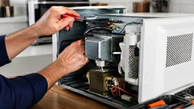 Manos utilizando un destornillador en el interior de un horno microondas abierto, con componentes y cables visibles.
