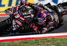 Piloto de MotoGP inclinado sobre su moto durante una curva, con el casco y el carenado en primer plano.