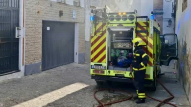 Un bombero junto a la parte trasera de un camión de extinción con mangueras desplegadas en una calle estrecha.