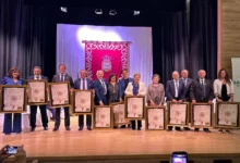 Grupo de personas sobre un escenario mostrando diplomas enmarcados durante una ceremonia.