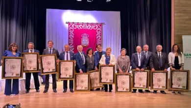 Grupo de personas sobre un escenario mostrando diplomas enmarcados durante una ceremonia.