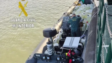 Agente de la Guardia Civil Marítima junto a numerosas garrafas blancas de combustible a bordo de una embarcación.