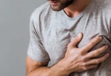 Primer plano del torso de un hombre con camiseta gris que mantiene una mano apoyada sobre el pecho.