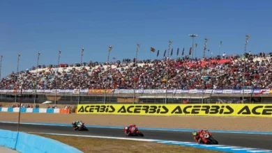 Tres motos de competición circulan por una curva del circuito ante las gradas llenas de espectadores.