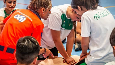 Varias jóvenes practican compresiones torácicas sobre un maniquí de reanimación mientras una profesional con ropa naranja del 061 supervisa la actividad.