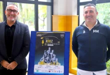 Dos hombres posan junto a un cartel de la XXX Media Maratón de Jerez 2026 en una sala con grandes ventanales.