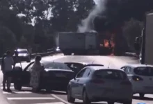 Varios turismos detenidos en una carretera mientras un camión desprende humo y presenta llamas en la zona trasera.