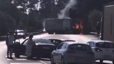 Varios turismos detenidos en una carretera mientras un camión desprende humo y presenta llamas en la zona trasera.