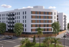 Recreación arquitectónica de un conjunto de edificios residenciales blancos con balcones oscuros, árboles, palmeras y calles con vehículos.
