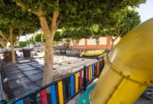 Parque infantil de la plaza de Las Alegrías con suelo de losetas, árboles, vallado de colores y un tobogán amarillo durante las obras.