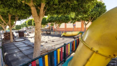 Parque infantil de la plaza de Las Alegrías con suelo de losetas, árboles, vallado de colores y un tobogán amarillo durante las obras.