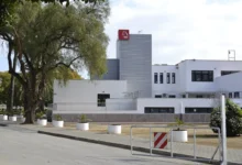 Exterior del Edificio Jerez 2002, con fachada blanca, torre de revestimiento metálico gris, árboles y maceteros junto a la acera.