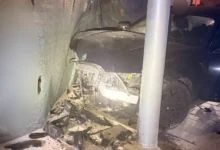 Frontal de un coche oscuro con daños graves tras impactar contra una estructura y una columna.