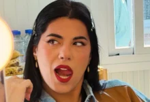 Primer plano de una mujer de cabello oscuro, con pendientes dorados y labios rojos, mirando hacia un lado con la boca abierta.