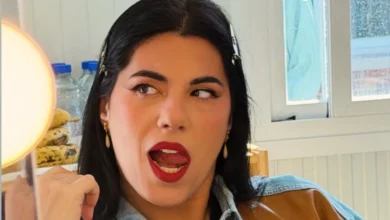 Primer plano de una mujer de cabello oscuro, con pendientes dorados y labios rojos, mirando hacia un lado con la boca abierta.