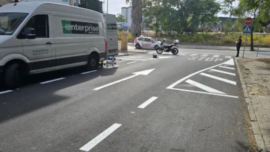 Calle asfaltada con flechas de circulación, señal de stop, furgoneta blanca y dos motocicletas junto a un paso peatonal.