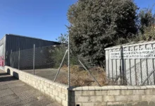 Antiguo Centro de Mayores de la Fundación Paz y Aflicción en Jerez, con parcela vallada, vegetación seca y edificio al fondo.