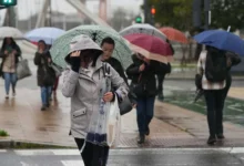 Varios peatones caminan bajo paraguas de distintos colores por una calle mojada mientras llueve.