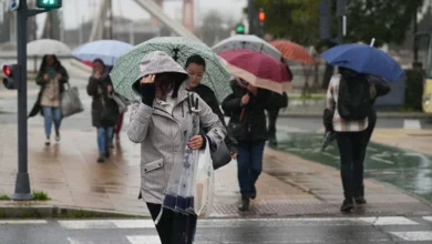 Varios peatones caminan bajo paraguas de distintos colores por una calle mojada mientras llueve.