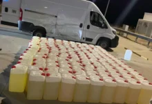 Petacas de gasolina alineadas en primer plano junto a una furgoneta blanca con daños visibles en un lateral, de noche.