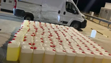 Petacas de gasolina alineadas en primer plano junto a una furgoneta blanca con daños visibles en un lateral, de noche.