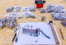 Herramientas, bolsas de tornillos, piezas metálicas y un dibujo impreso de un barco infantil con tobogán sobre un tablero de madera.