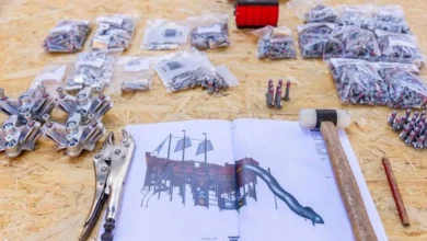 Herramientas, bolsas de tornillos, piezas metálicas y un dibujo impreso de un barco infantil con tobogán sobre un tablero de madera.