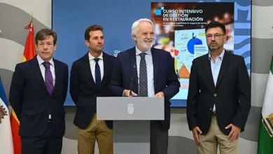 Cuatro hombres posan ante un atril institucional en una sala con banderas y una pantalla sobre un curso intensivo de gestión en restauración.