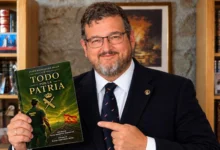 Hombre con gafas, barba y traje oscuro que sostiene un ejemplar del libro Todo por la Patria, de Jesús Rodríguez Arias, y señala su cubierta.