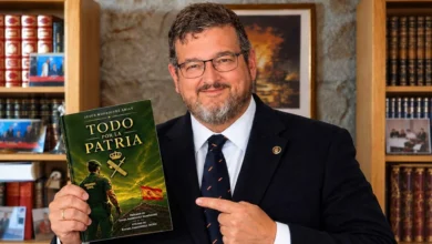 Hombre con gafas, barba y traje oscuro que sostiene un ejemplar del libro Todo por la Patria, de Jesús Rodríguez Arias, y señala su cubierta.