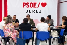 Varias personas sentadas alrededor de una mesa durante una reunión, con una pancarta del PSOE de Jerez al fondo.