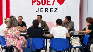 Varias personas sentadas alrededor de una mesa durante una reunión, con una pancarta del PSOE de Jerez al fondo.