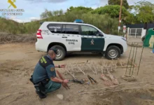 Agente de la Guardia Civil agachado junto a redes, cuerdas, varillas y herramientas colocadas en el suelo, con un vehículo del SEPRONA al fondo.