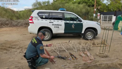 Agente de la Guardia Civil agachado junto a redes, cuerdas, varillas y herramientas colocadas en el suelo, con un vehículo del SEPRONA al fondo.