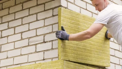 Trabajador con guantes oscuros colocando un panel amarillo de aislamiento térmico sobre una pared de bloques claros.