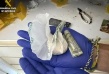 Manos con guantes azules sostienen envoltorios con una sustancia blanca en polvo y un billete enrollado.