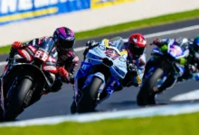 Tres pilotos de motociclismo compiten en una curva, con una moto negra y roja delante de otras dos motos azules.