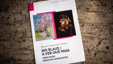 Cartel de la exposición Ins Blaue/A ver qué pasa de Abena Bauer y Sebastian Gessenharter sobre una mesa de madera