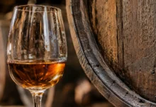 Primer plano de una copa de vino de Jerez ámbar junto a la textura de una barrica de madera.