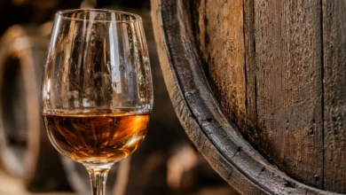 Primer plano de una copa de vino de Jerez ámbar junto a la textura de una barrica de madera.