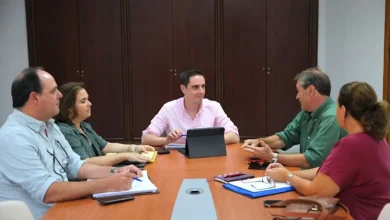 Reunión de varias personas sentadas alrededor de una mesa con documentación, dispositivos electrónicos y una tableta.
